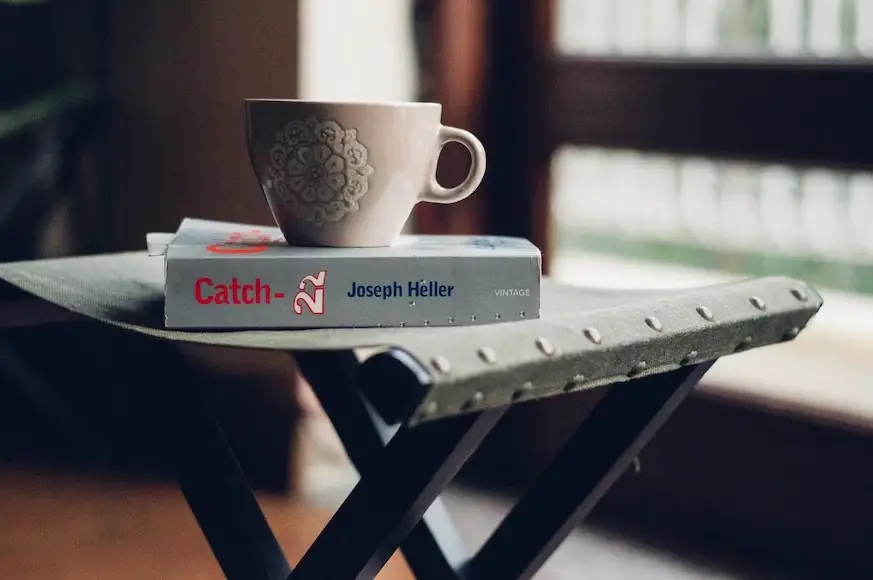 A cup of coffee placed on top of a book with the title Catch 22.