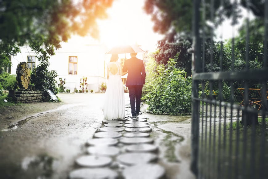 Newly-wed couples walking together over circular pavements while holding an umbrella.