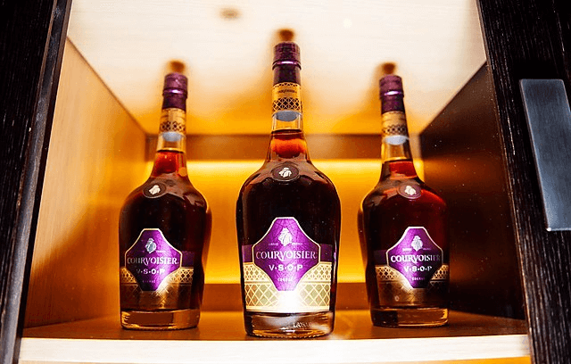 Three bottles of courvoisier in a well lighted storage cabinet.
