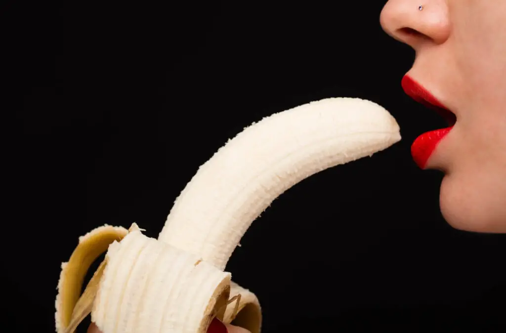 A woman with red lipstick putting a banana in her mouth.