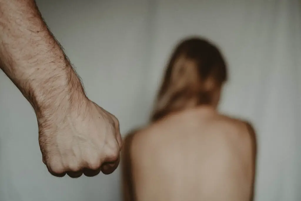 A man clenching his fist approaching a woman sitting down back-naked.