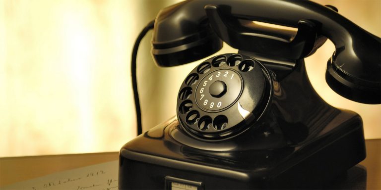 A black, rotary dial phone with numbers.