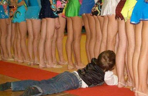 A kid crawling into a red carpet approaching a group of ladies in mini skirt.