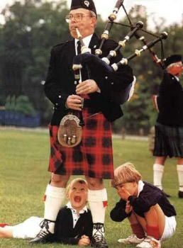 Two kids peep into the skirt of a Scottish bagpiper.