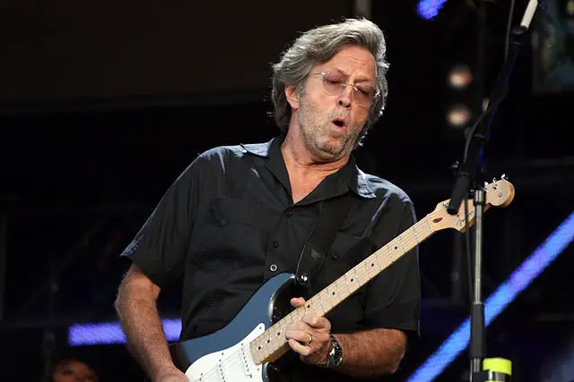 Eric Clapton playing his guitar on stage while singing.