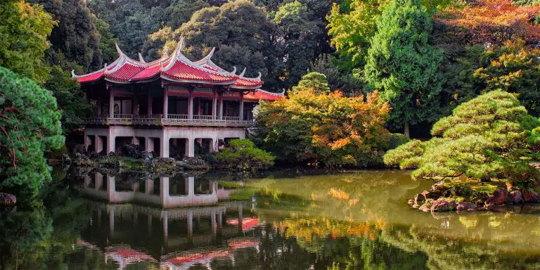 A traditional Japanese Pagoda built in front of a calm lake surrounded by trees.