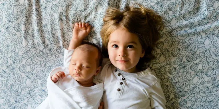A baby child lying on a bed with his older sister.