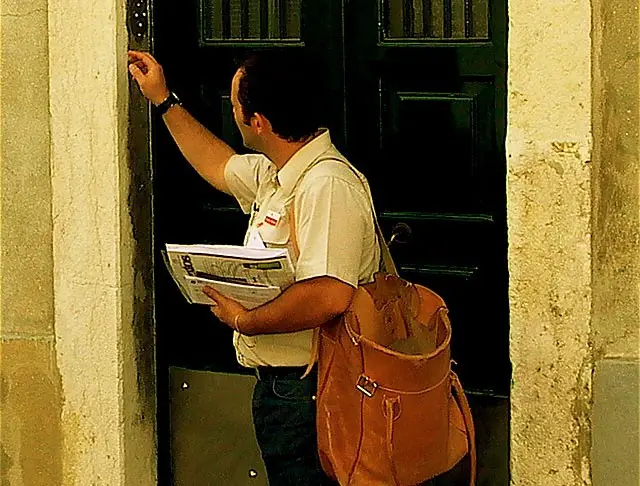A postman with his bag delivering mails at the door.
