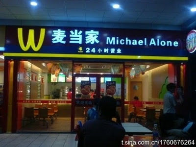 People eating in front of the restaurant Michael Alone, which borrows a logo of the "M" in McDonald's but upside down.