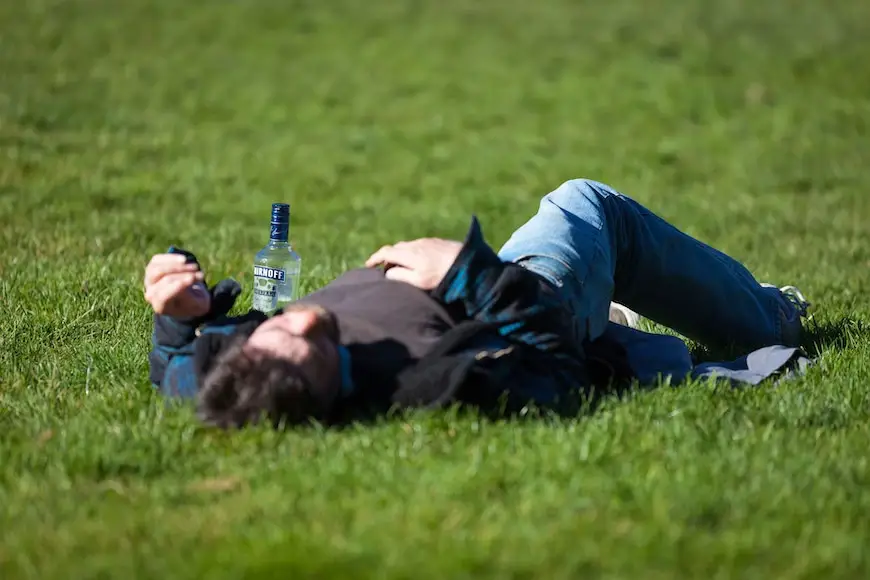 Drunk man with his Smirnoff bottle lying on the grass during the middle of the day.