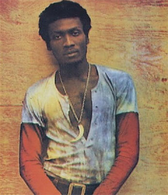 Jimmy Cliff in a white T-shirt standing against a wall.