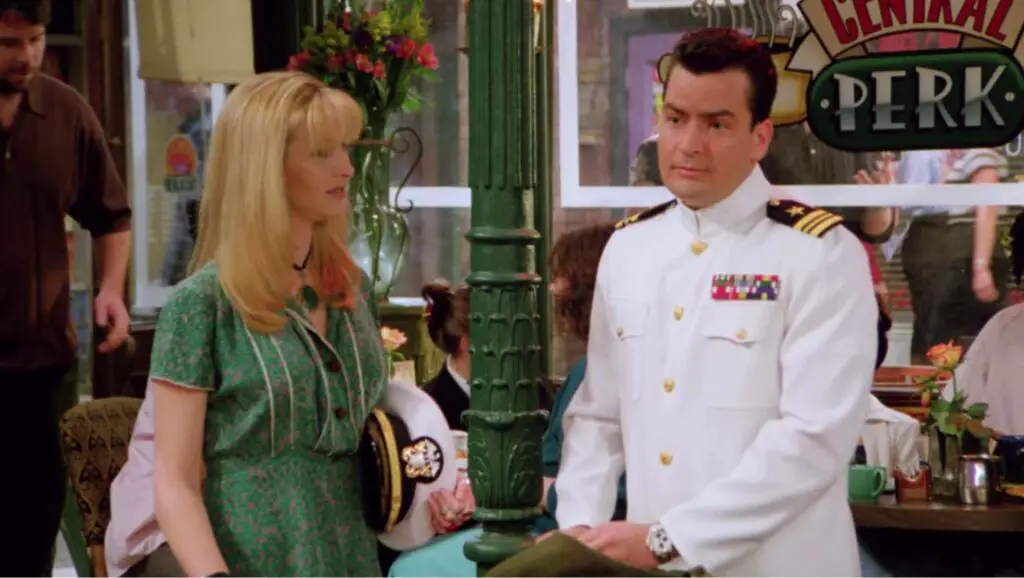 Charlie Sheen in a white navy uniform with another actress wearing green dress.