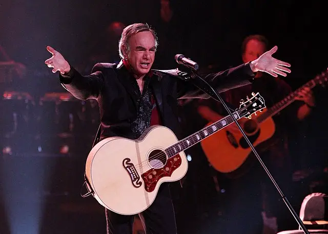 Neil Diamond with a guitar performing on stage.