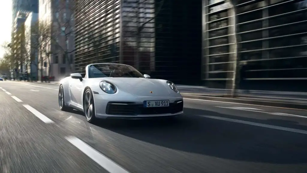 A grayish white Porsche sports car speeding in urban streets.
