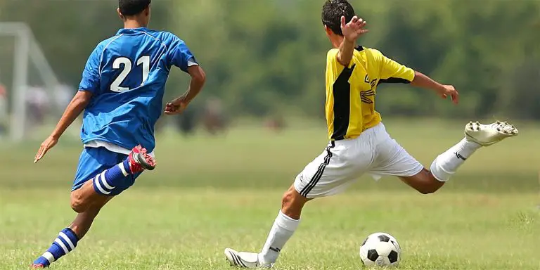 A soccer player in yellow shirt tries to kick the ball while his opponent in blue tries to steal it.