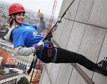 A woman wearing a helmet and harness abseilling outside the building.