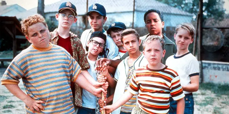 Nine young kids make a pose in the field while holding a baseball bat.