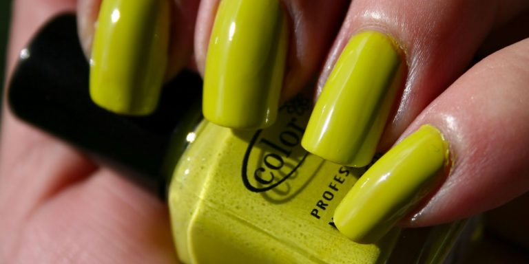 A hand with yellow green finger nails holding a yellow green nail polish.