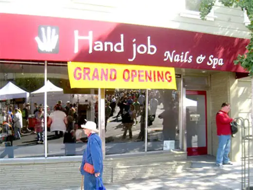 An elderly woman passing in front of the newly-opened business, Hand Job Nails and Spa.
