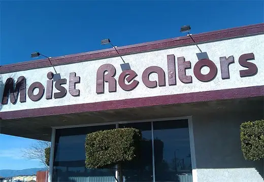A sign at the top of a real estate business that says Moist Realtors.