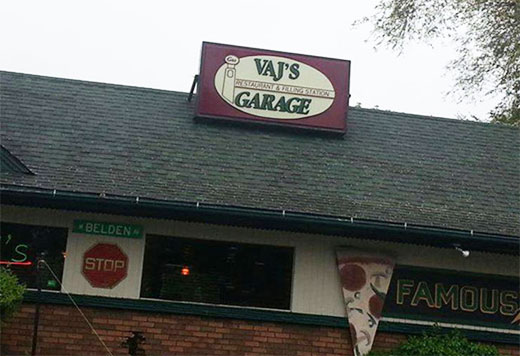 A sign at the rooftop of a business that says, "Vaj's Garage restaurant and filling station."