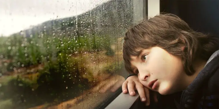 A boy looking out the glass window feeling bored.