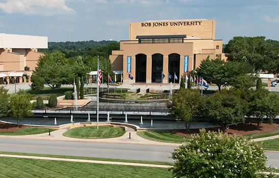 Flags and facade of Bob Jones University with a circular fountain on the front.