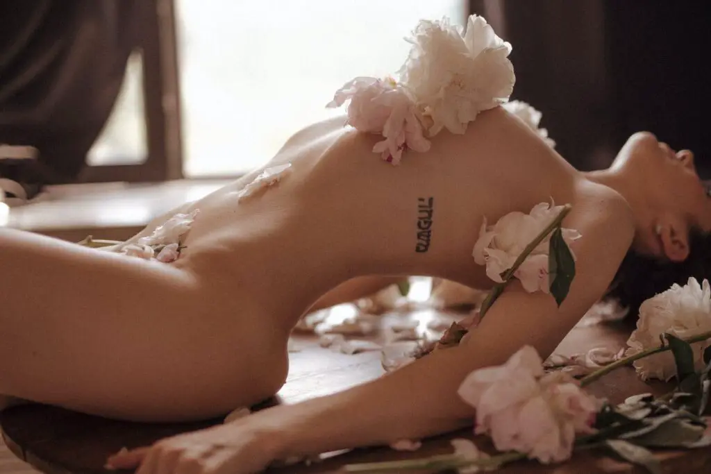 A sexy nude photo of a woman laying down with flowers covering parts of her body.